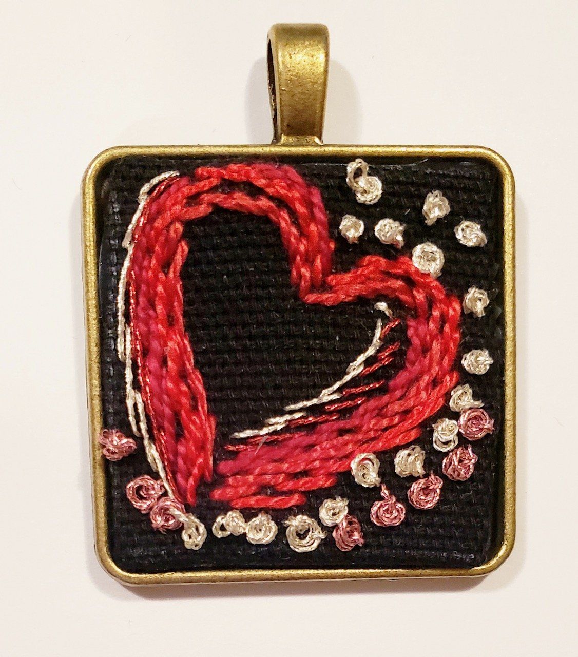 A square pendant with a red heart embroidered on it