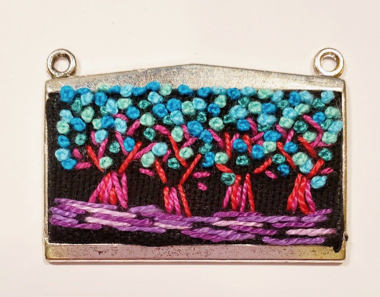 A pendant with a picture of trees embroidered on it