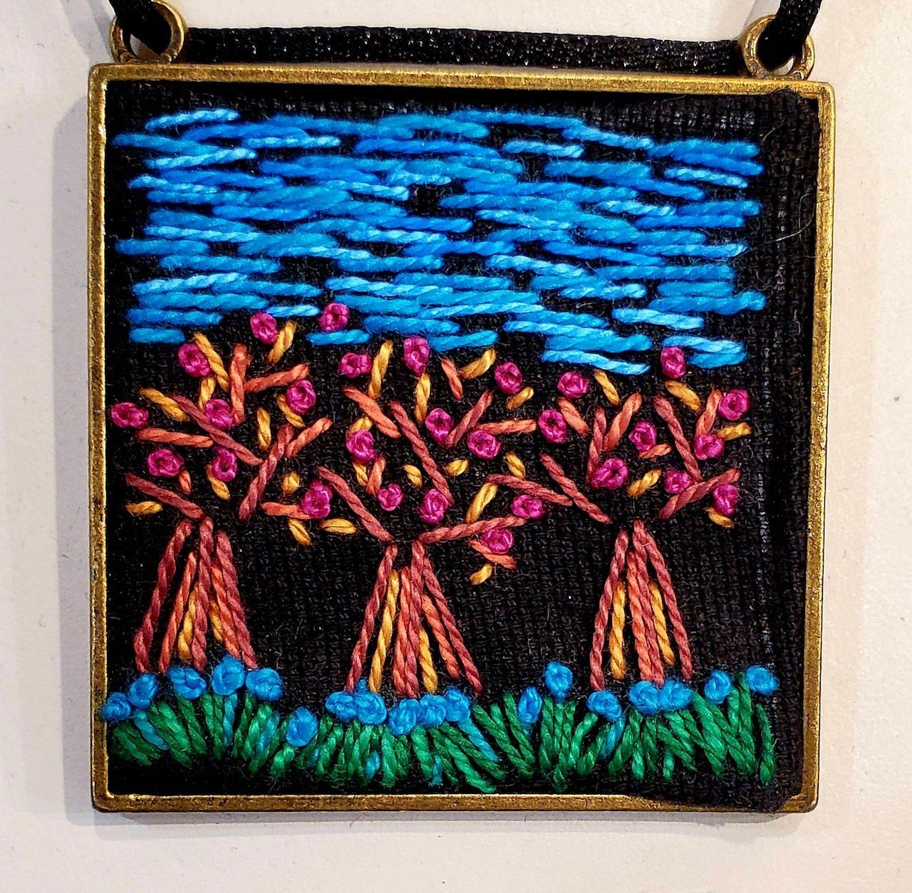 A necklace with three trees embroidered on it
