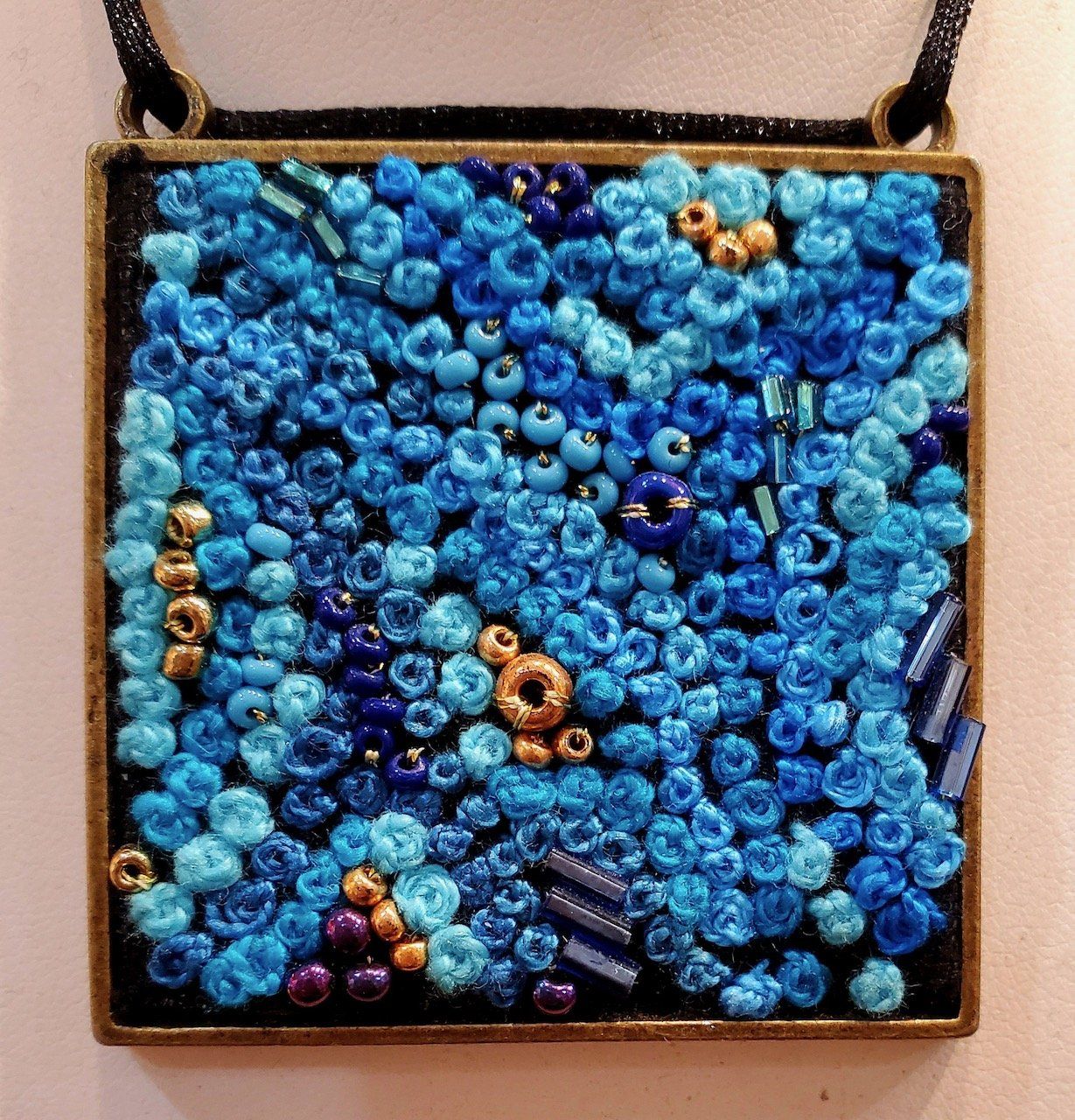 A square pendant with blue beads on it