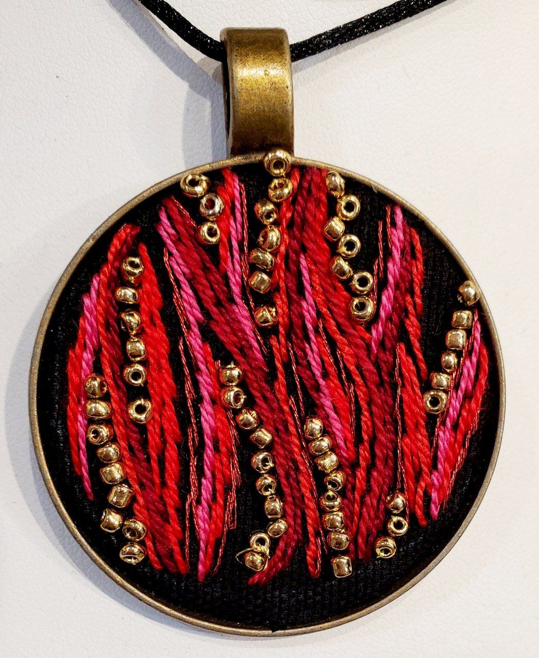 A red and black pendant with gold beads on a black cord