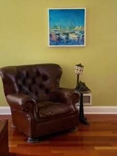 A living room with a brown leather chair and a painting on the wall.