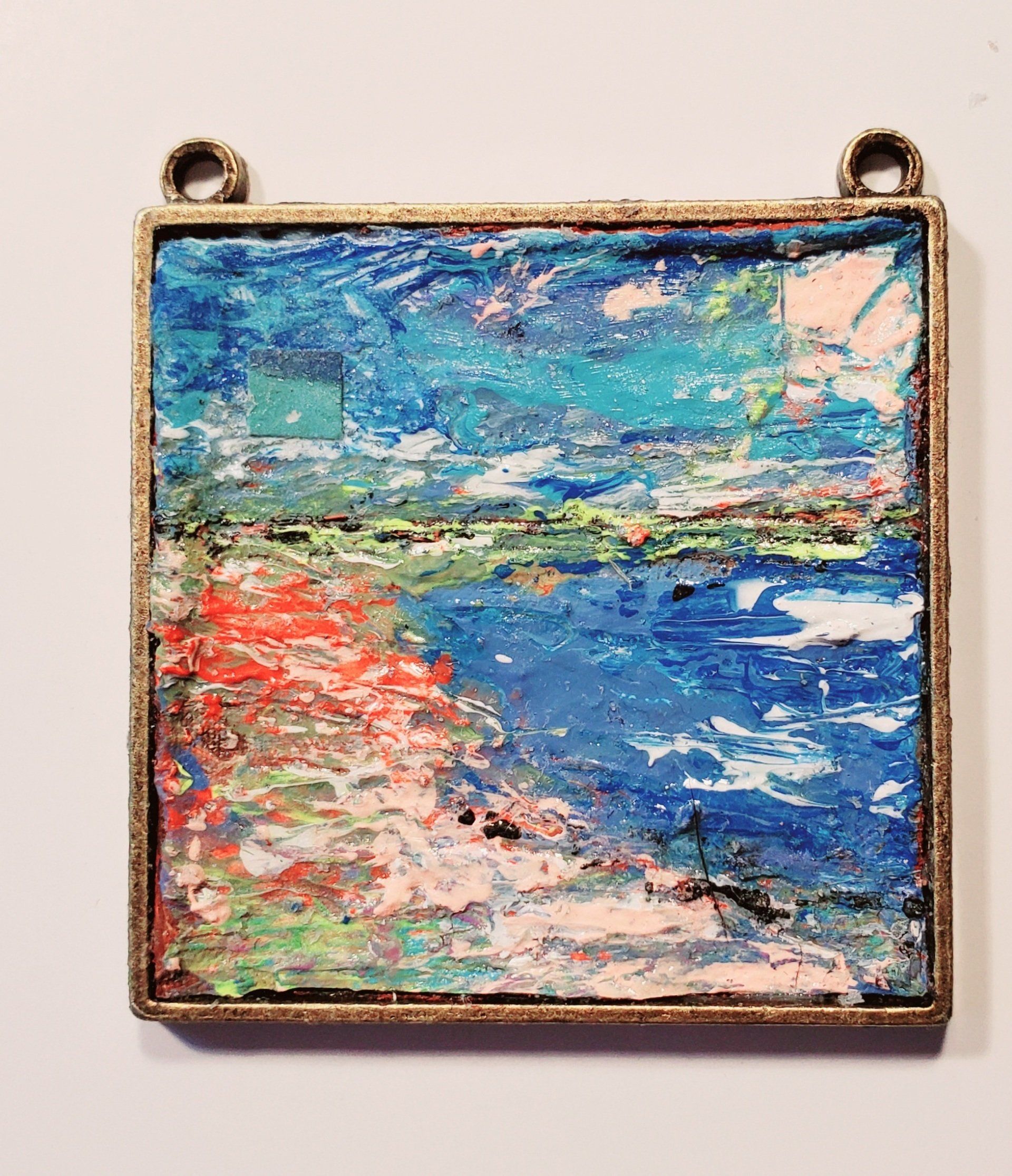 A square pendant with a painting on it