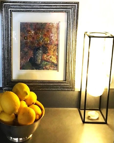 A bowl of lemons sits on a counter next to a painting