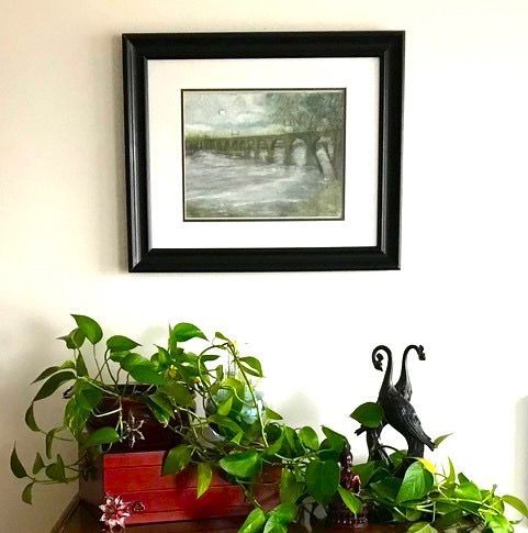 A picture of a bridge is hanging on a wall above a plant