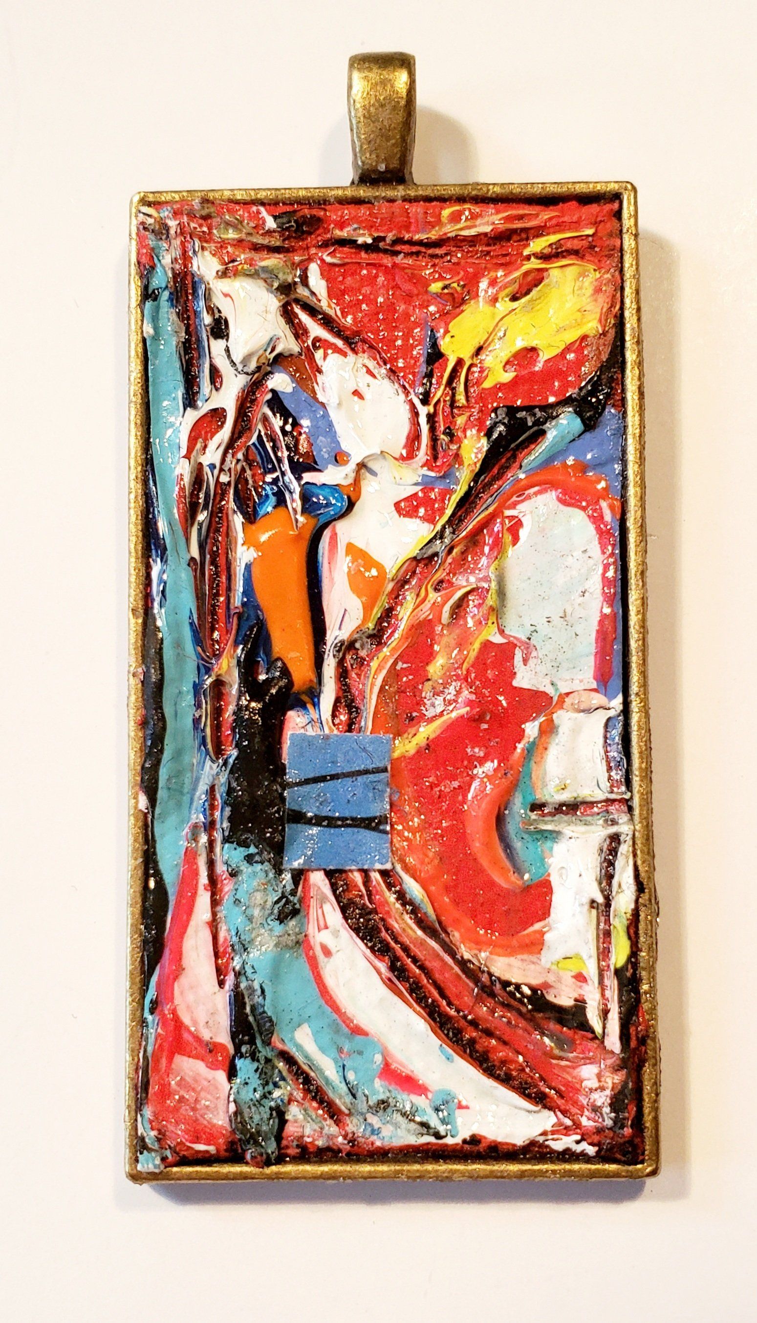 A pendant with a colorful painting on it is hanging on a white wall.