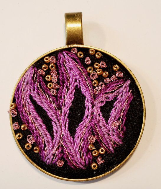 A pendant with purple embroidery on a black background