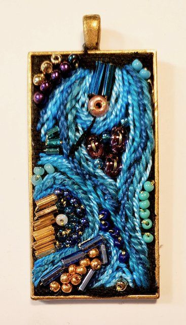 A blue and gold pendant with beads on a white surface.