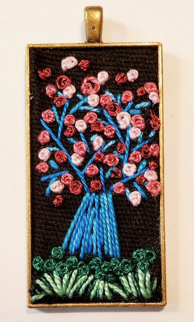 An embroidered picture of a vase of flowers on a black background