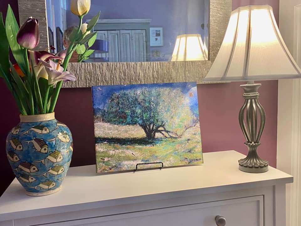 A vase of flowers is sitting on a table next to a lamp and a painting of a tree.