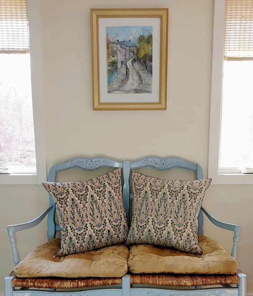 A bench with two pillows and a picture on the wall above it.