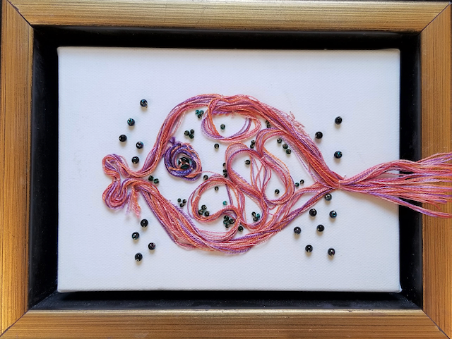A picture of a fish made of yarn and beads