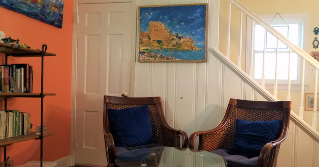 A living room with two chairs , a table and a painting on the wall.