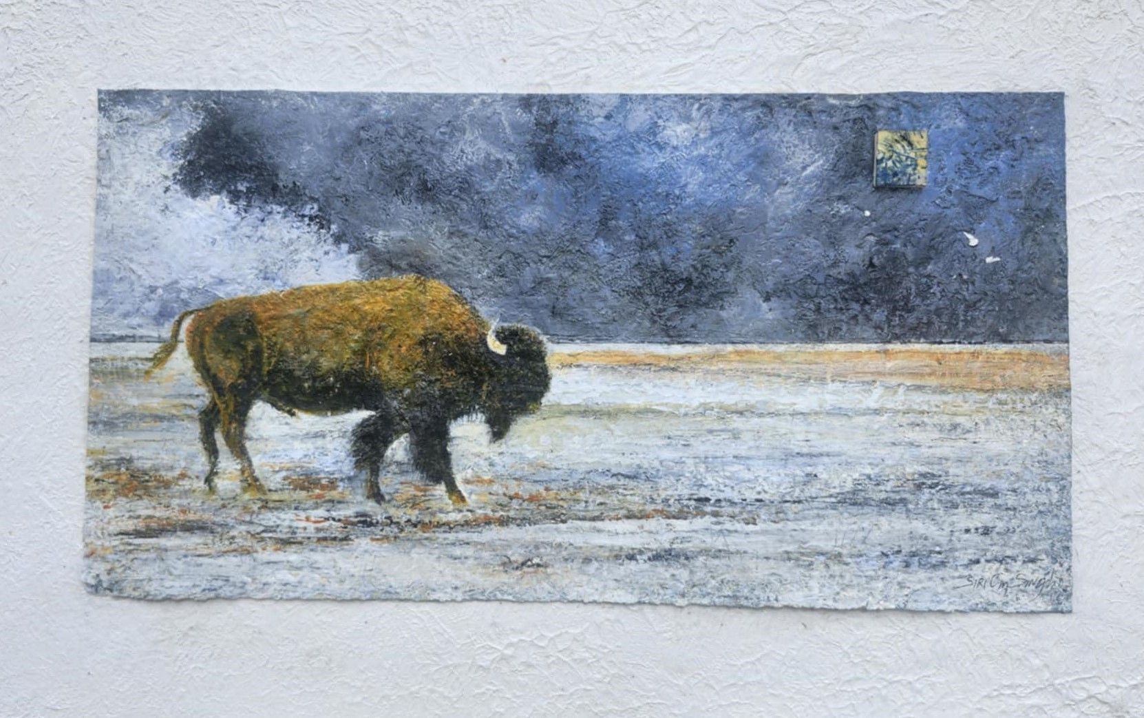 A man with a beard is standing in front of three paintings on a wall.