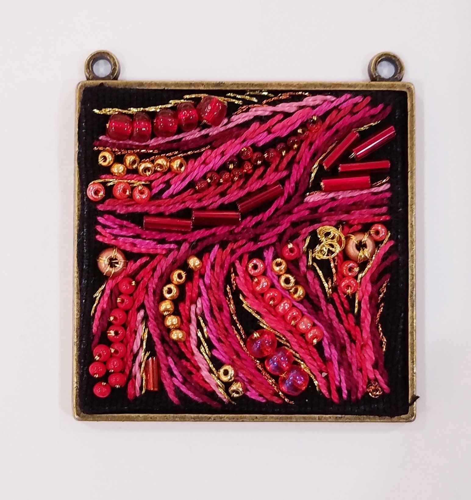 A square pendant with red and gold beads on it
