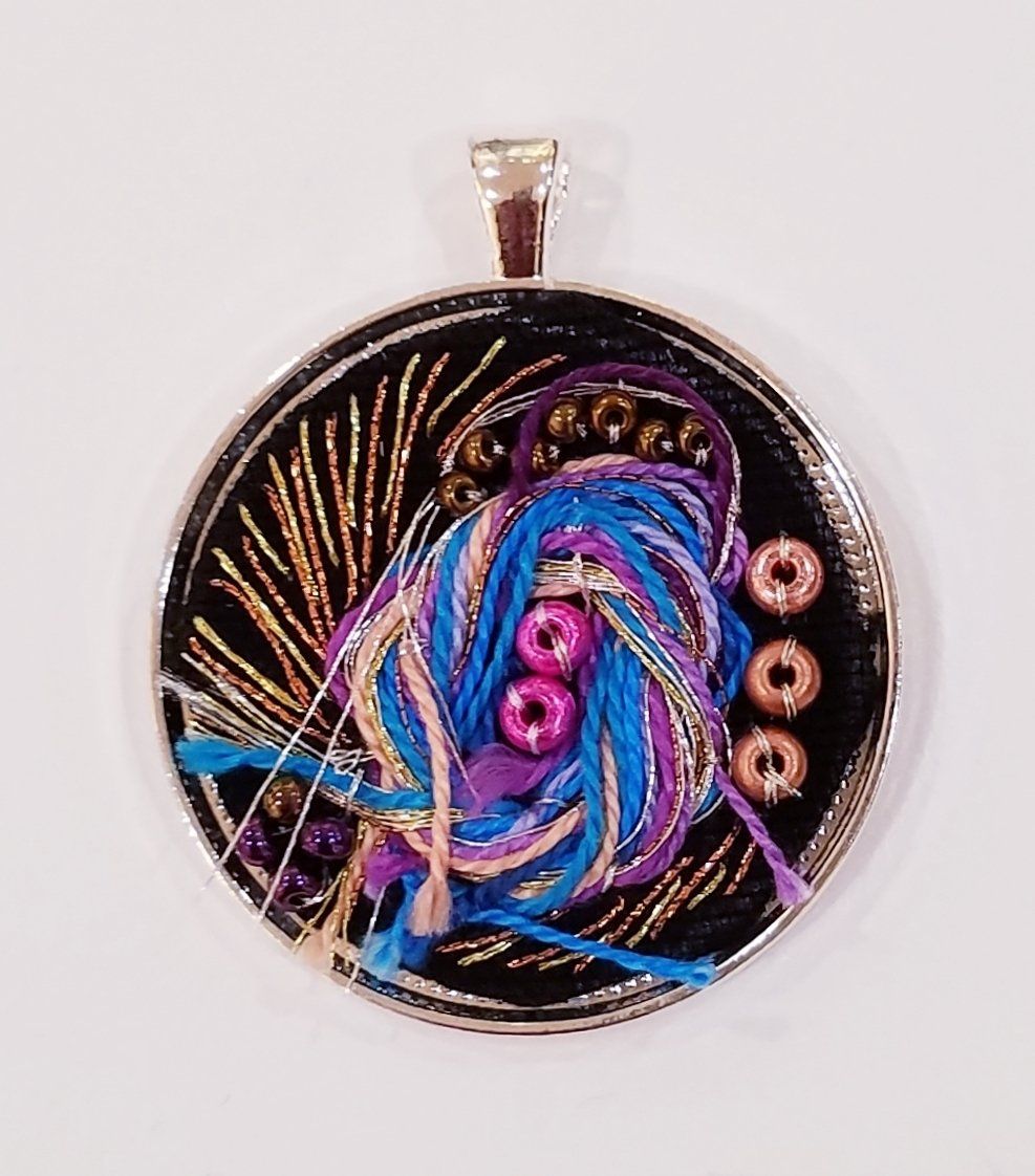 A round pendant with yarn and beads on it