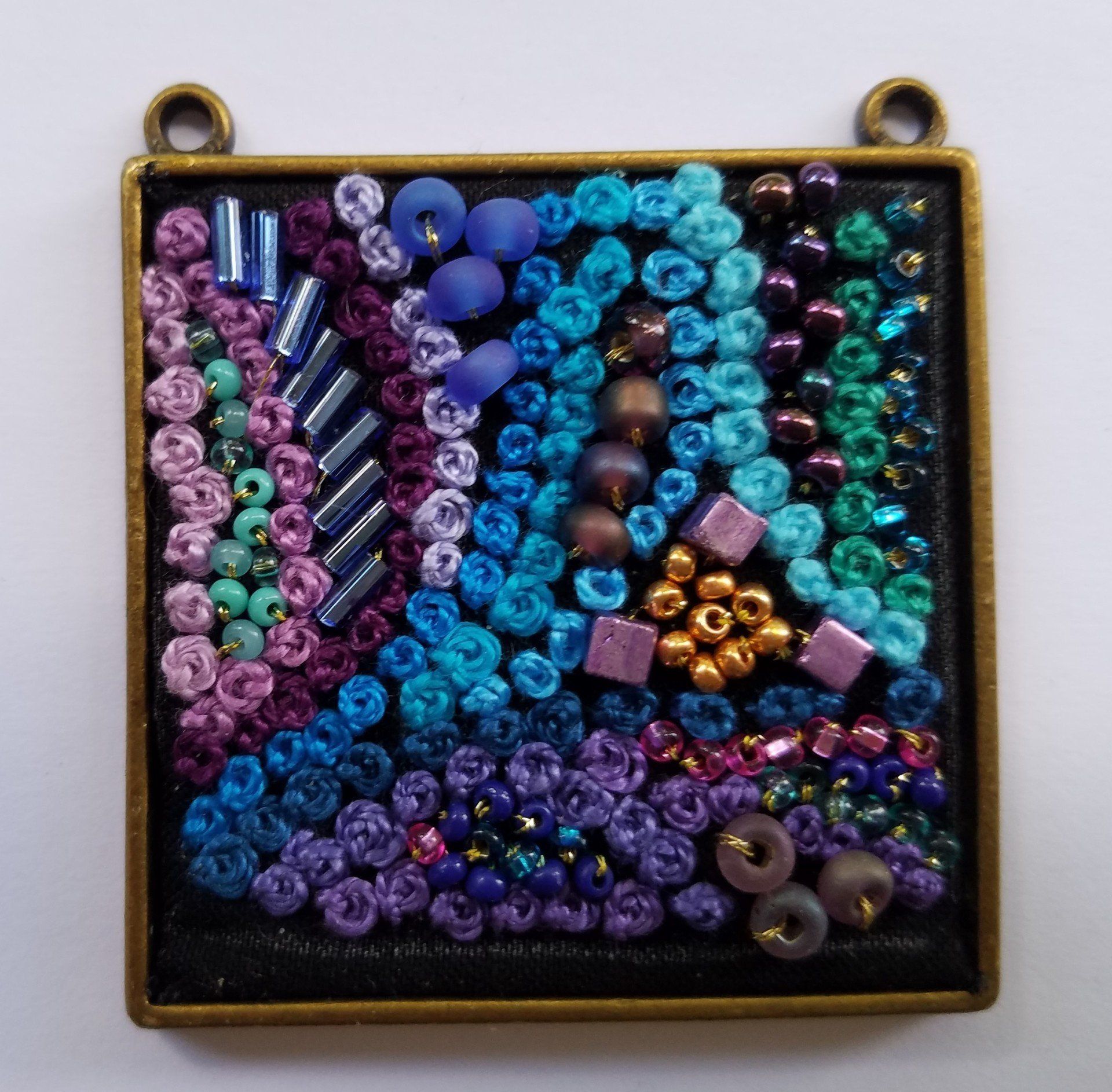 A square pendant with purple and blue beads on it