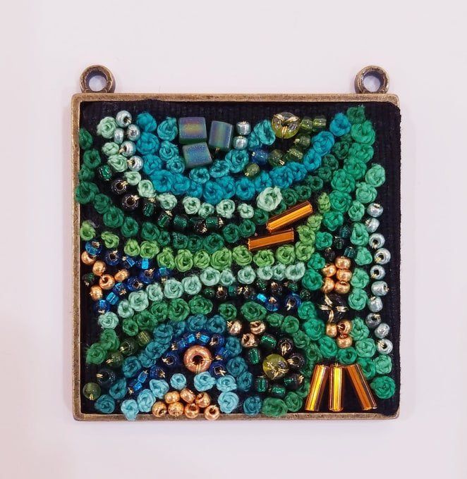 A square pendant with green and blue beads on it
