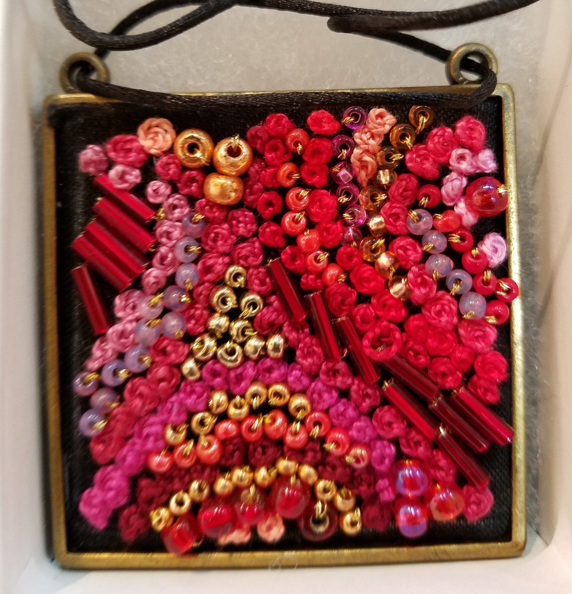 A square pendant with red and pink beads on it