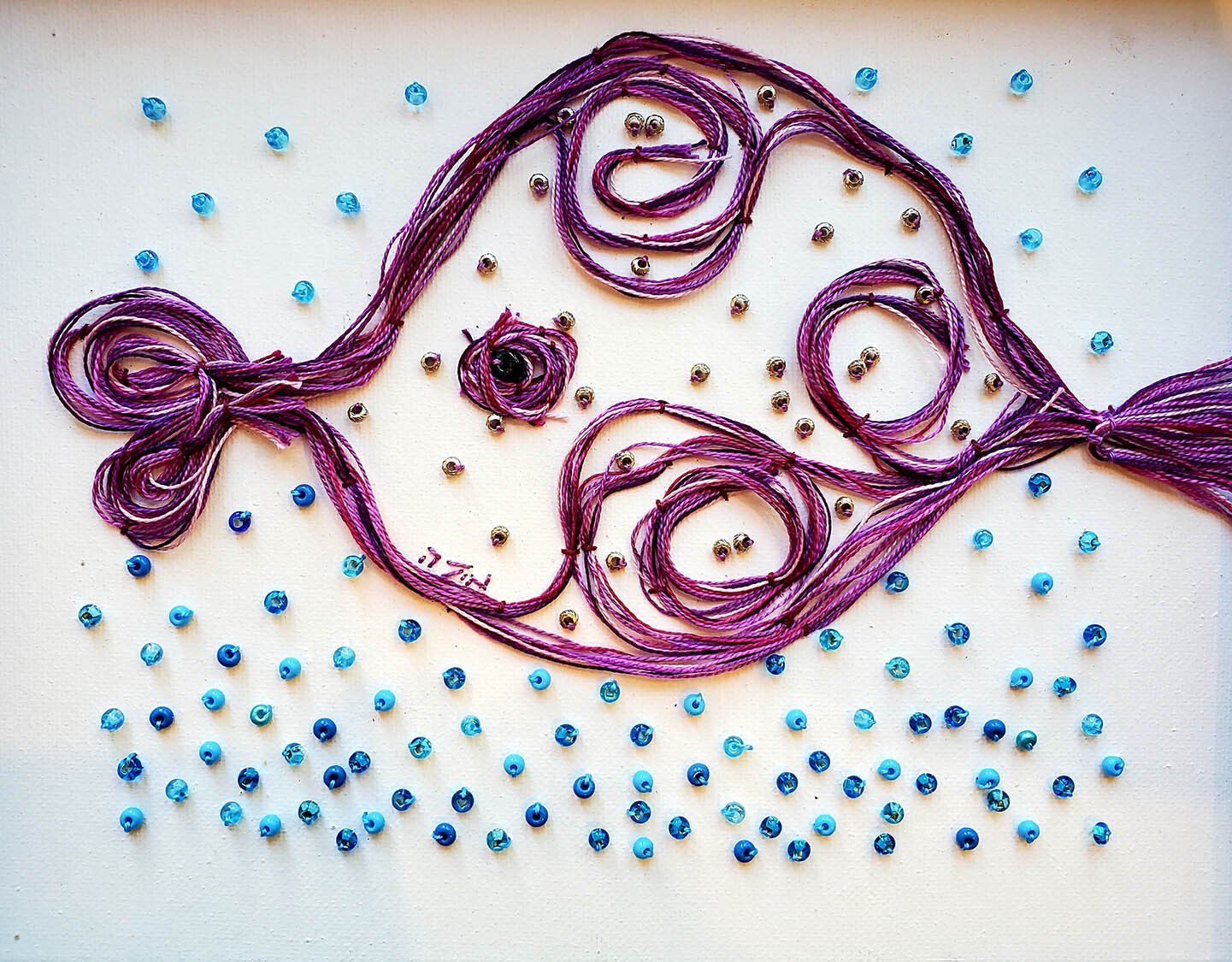 A purple fish is surrounded by blue beads on a white surface