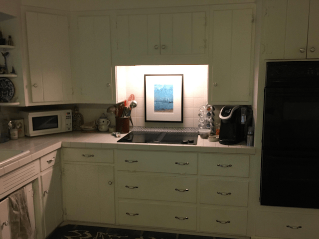 A kitchen with white cabinets and a picture on the wall