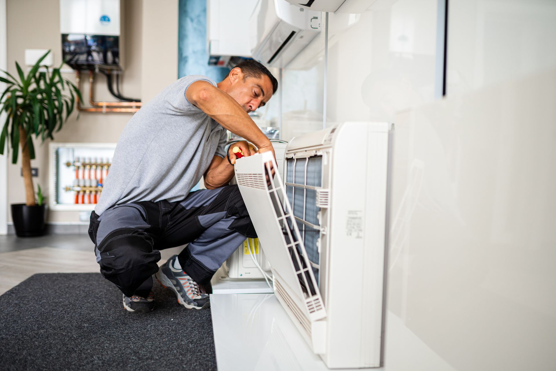 A Man Is Working On An Air Conditioner Near Wall - Normal, IL - Schulz Heating & Cooling