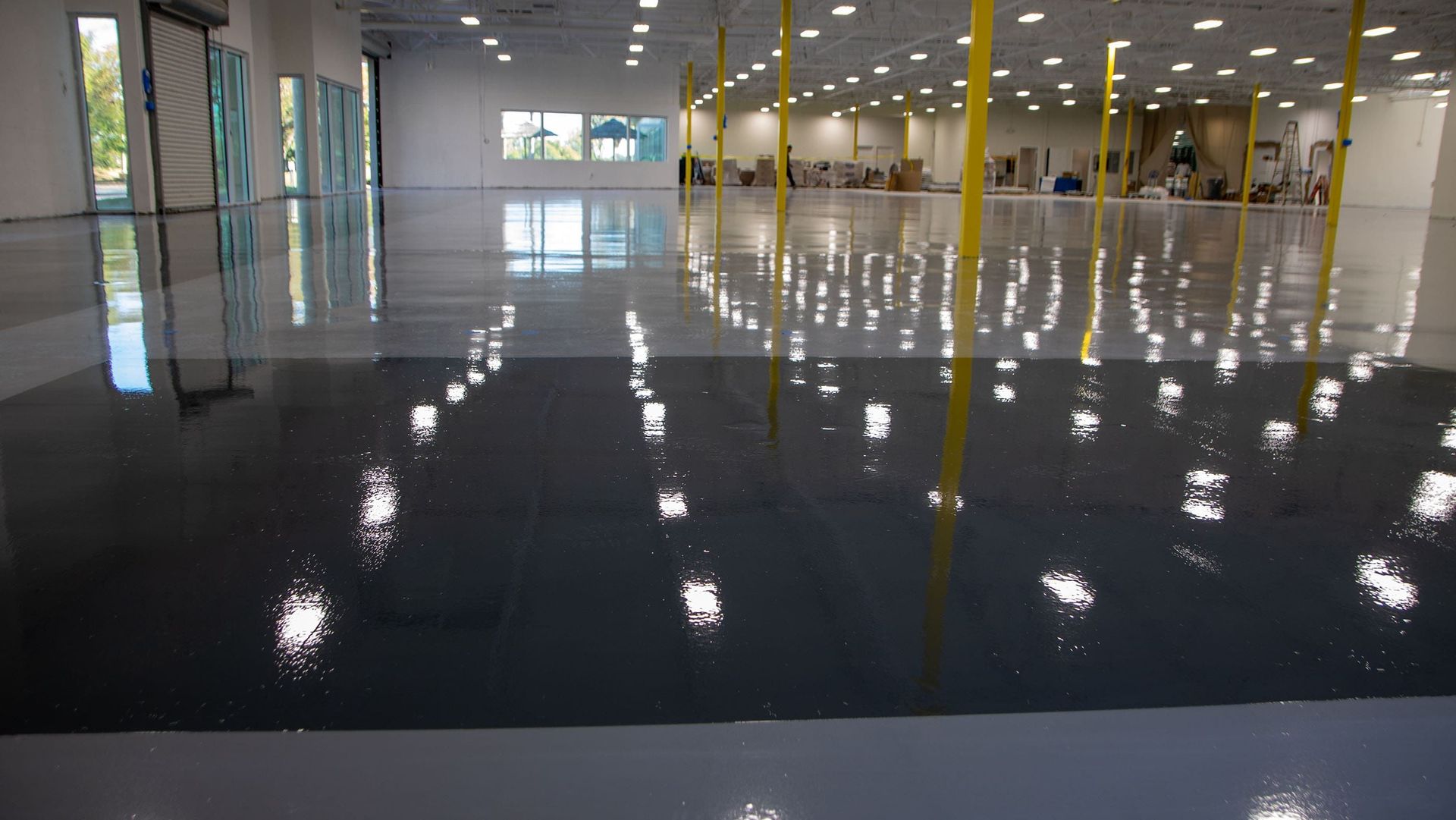 Glossy, gray and white epoxy floor in a large, empty commercial space reflecting overhead lights.