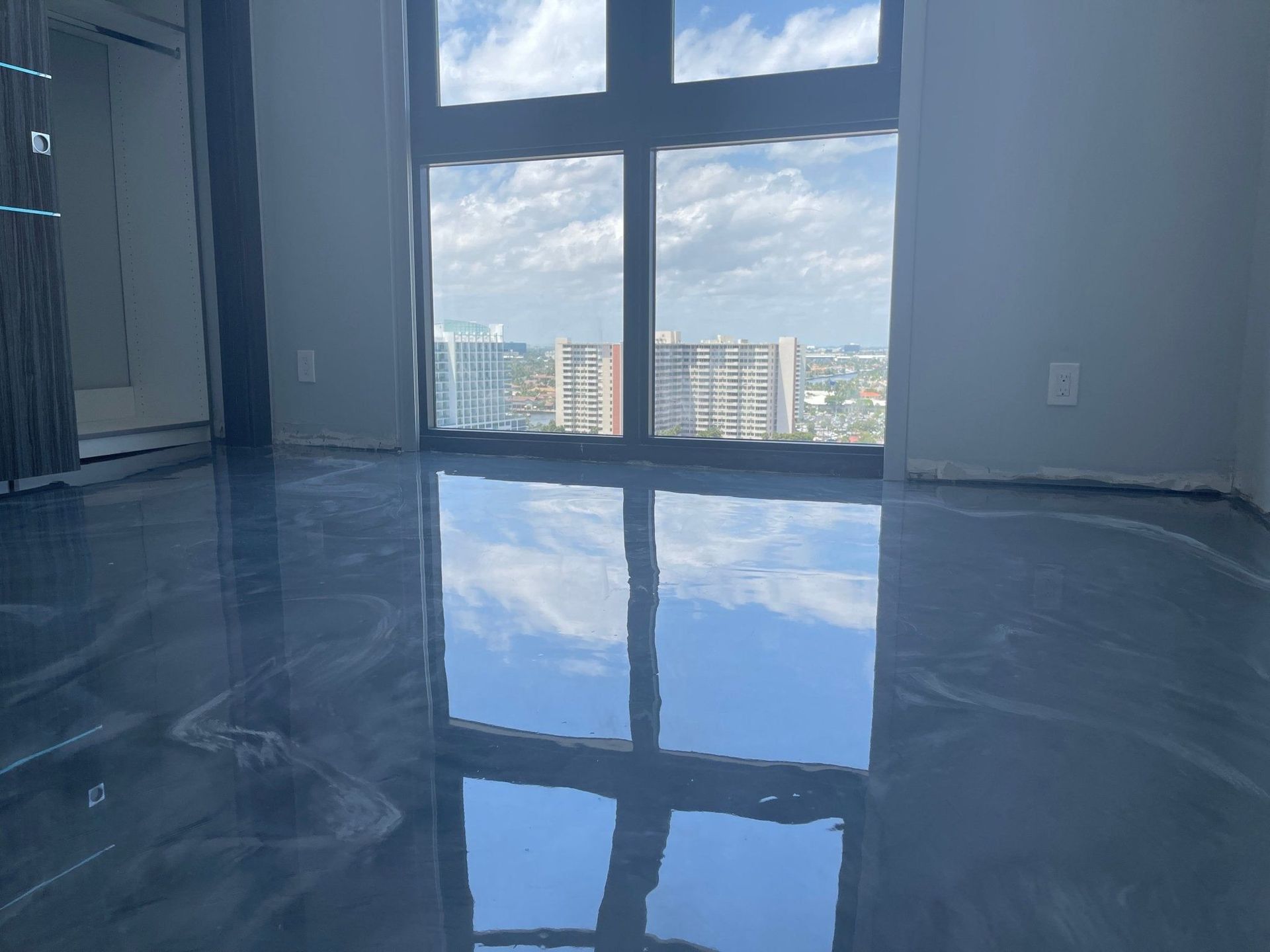 Shiny blue epoxy floor reflecting the view through a large window. Buildings and sky are visible.