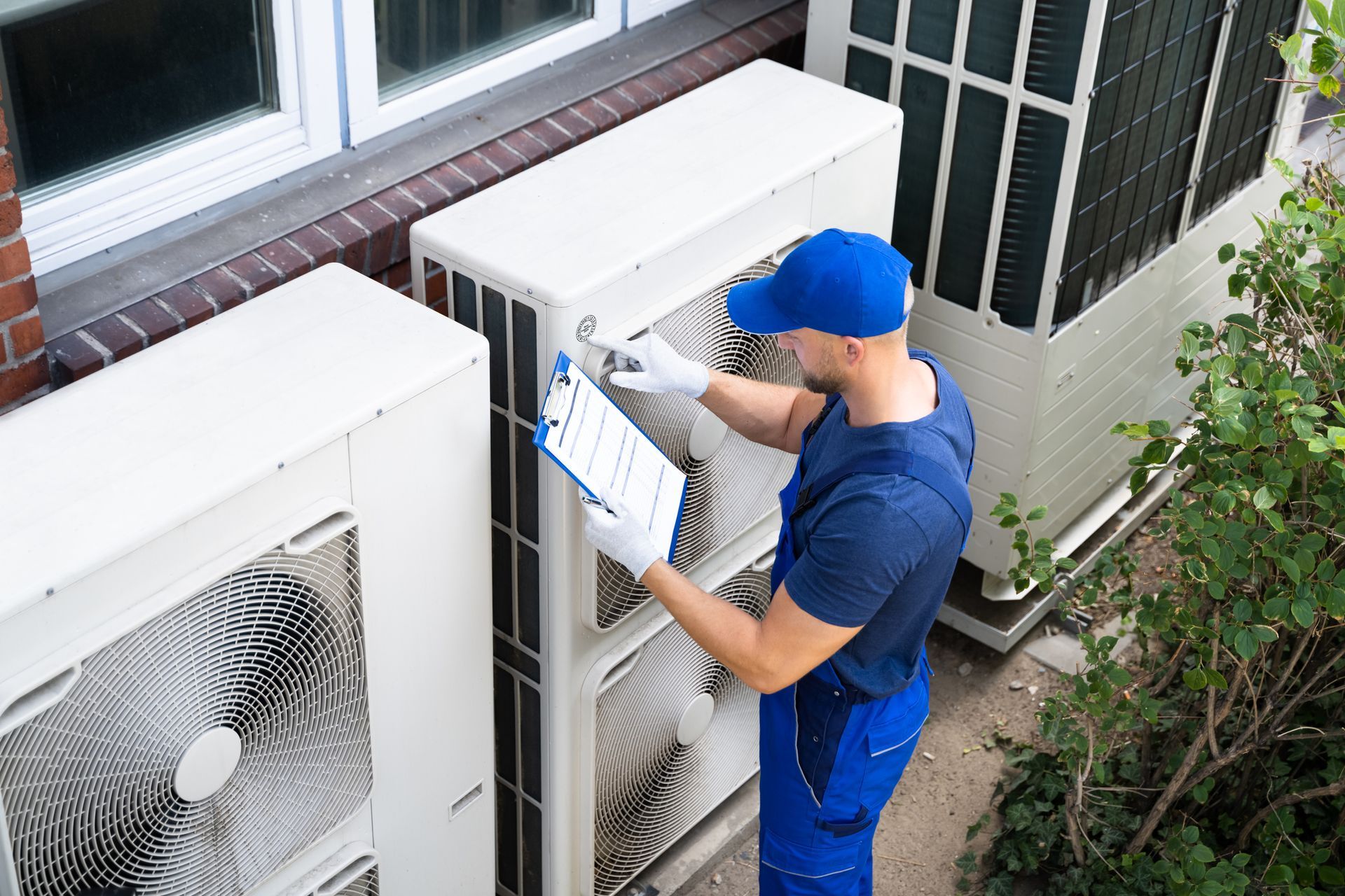 A Man Is Working On an Air Conditioner Outside of a Building — Independence, MO — McIntosh Heating & Cooling