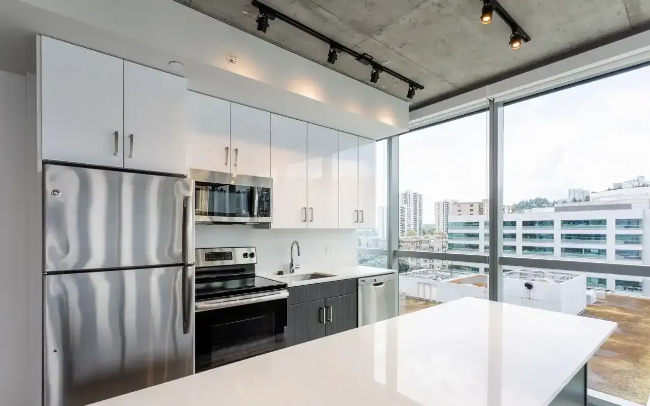 Modern kitchen with white cabinets, stainless steel appliances, and a large window view of the city.