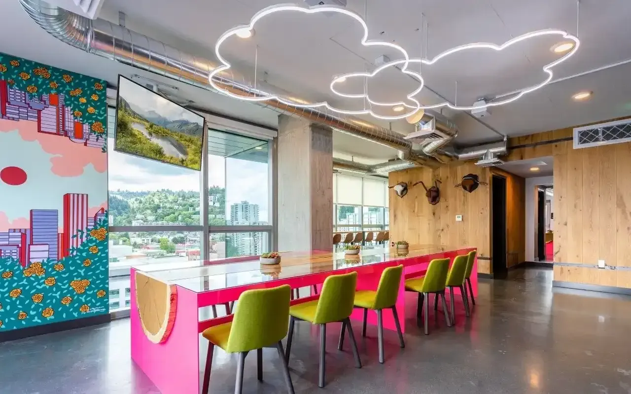 Conference room with pink table and green chairs, cloud-shaped light fixture, and city view.