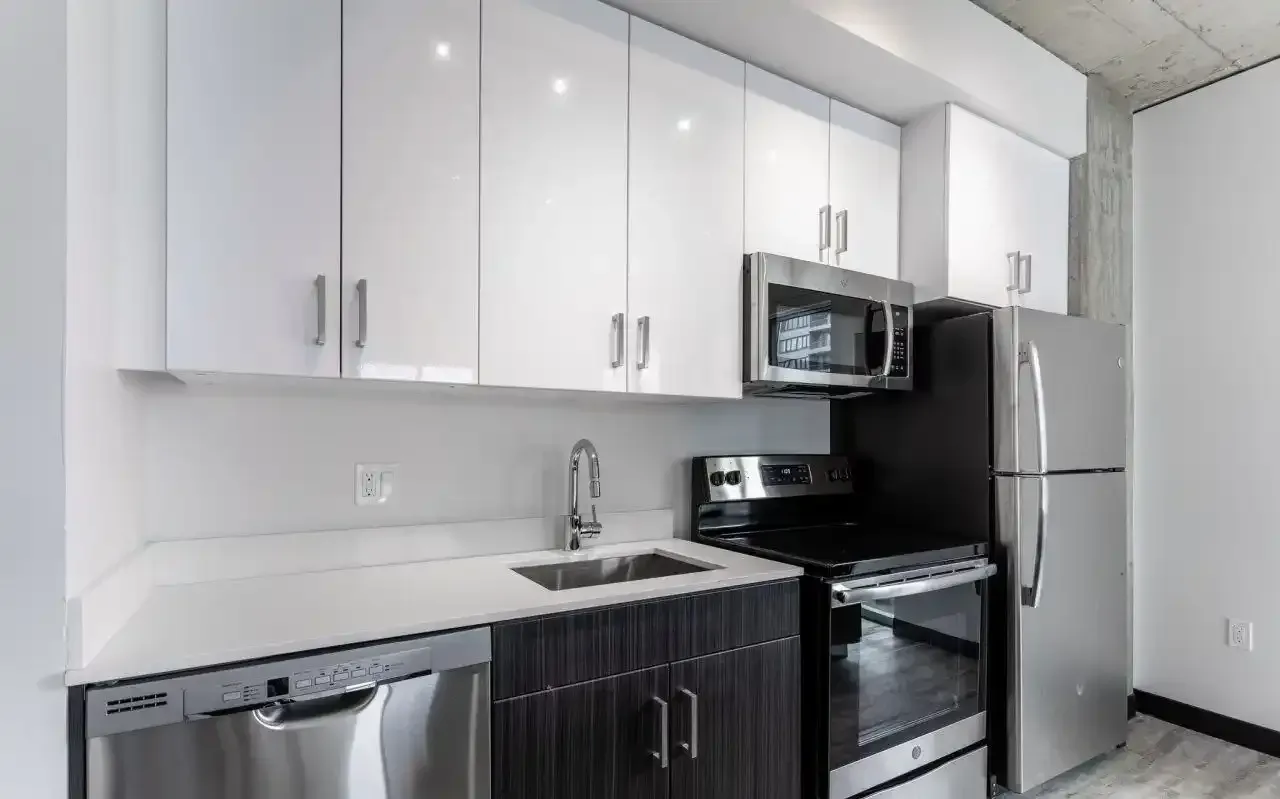 Modern apartment kitchen with white upper cabinets, dark lower cabinets, and stainless steel appliances.