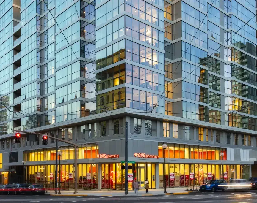 Modern glass building with a CVS store on the ground floor; cars and streetlights visible.