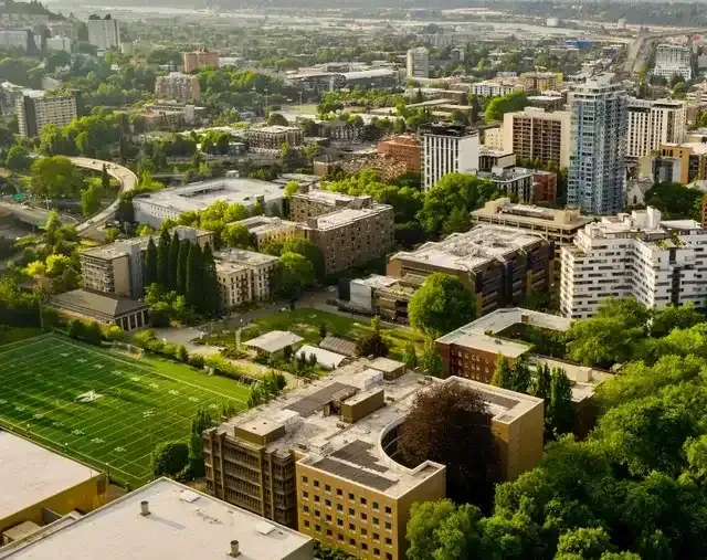 Aerial view of a city with buildings, green trees, and a football field.