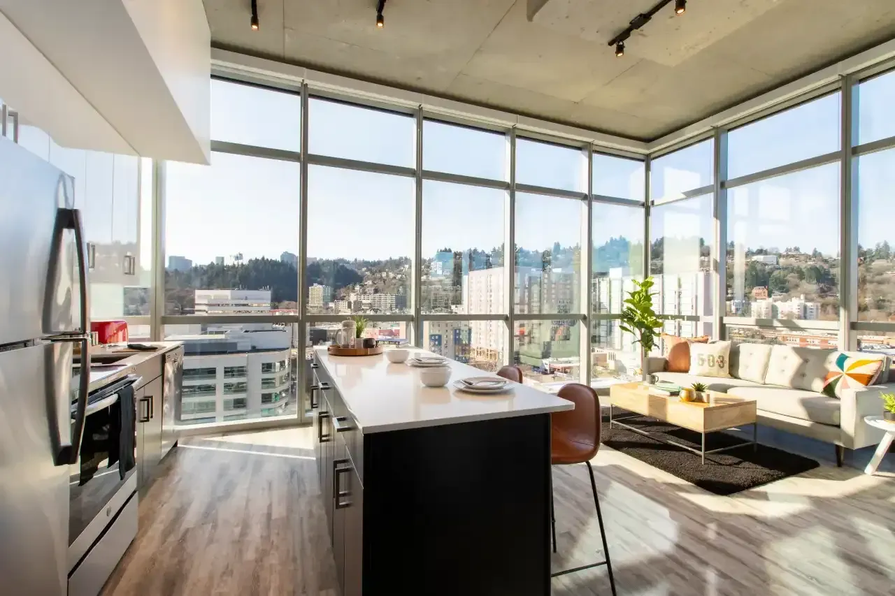 Modern kitchen with island, floor-to-ceiling windows showing a city view. Bright interior, open floor plan.