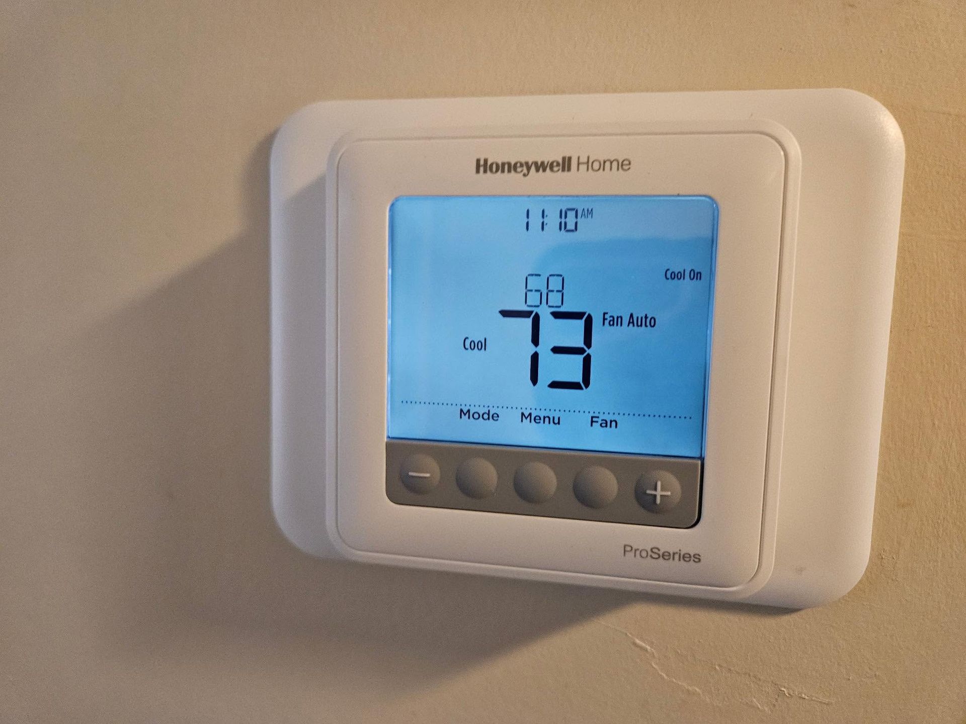 Honeywell Home digital thermostat mounted on a wall, displaying 73°F on a blue backlit screen.