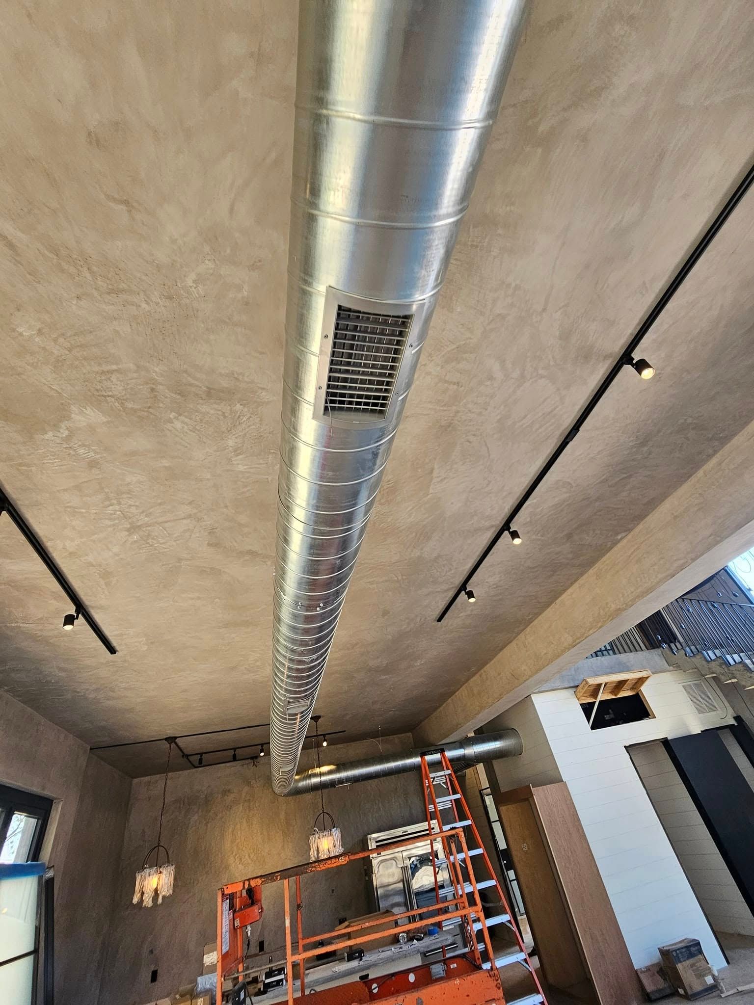 Ceiling-mounted silver ductwork over orange scaffolding in an unfinished room with track lights