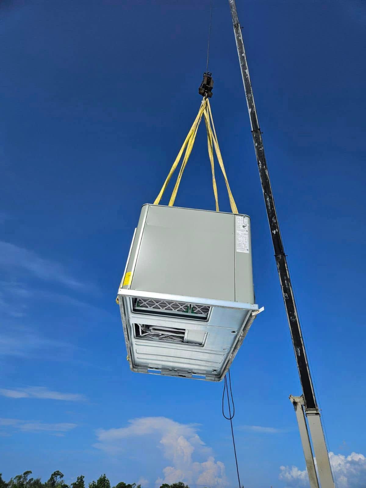Gray HVAC unit being lifted by yellow straps against a blue sky outdoors