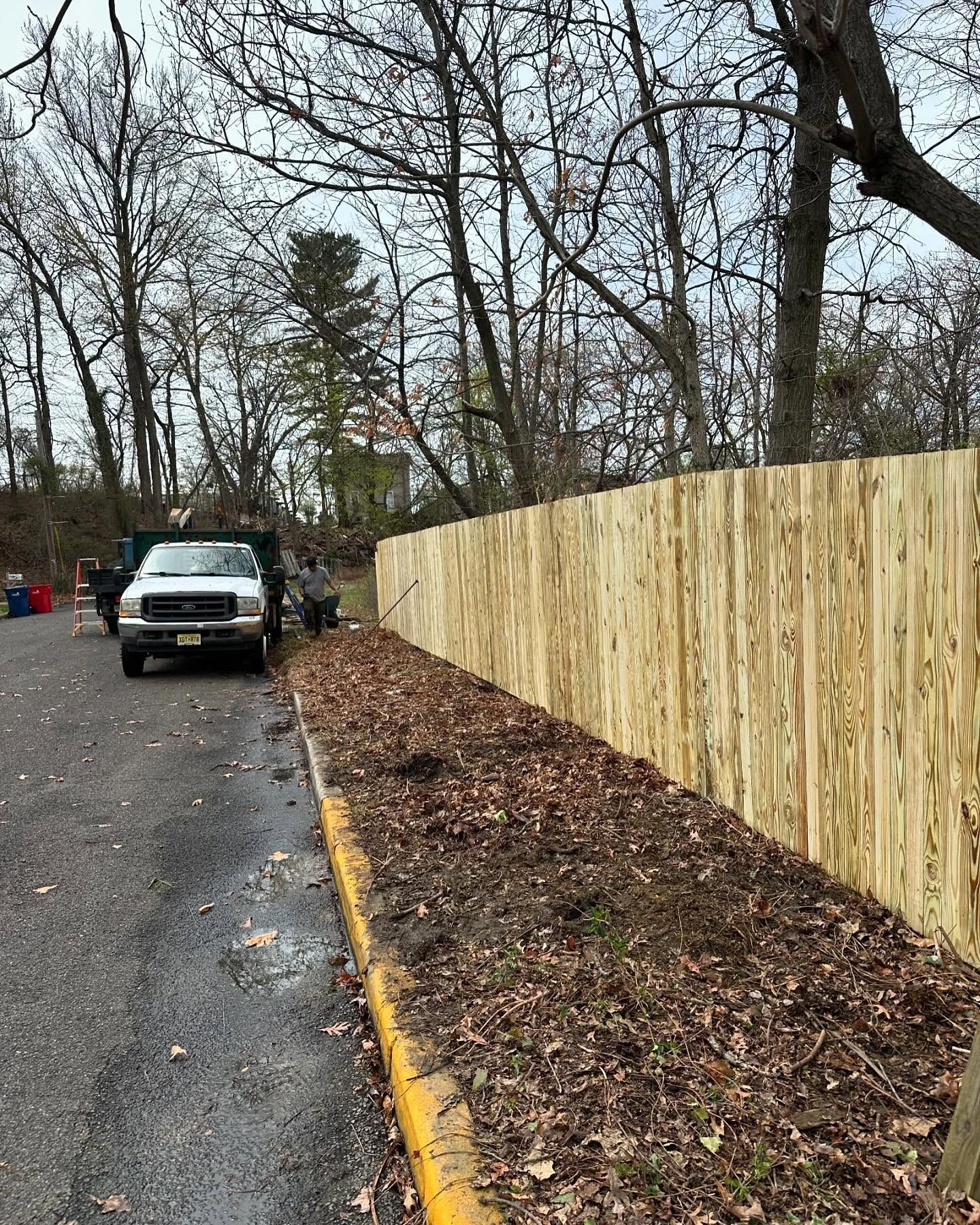 White picket fence gate in front of a building and trees on a paved surface under a cloudy sky.