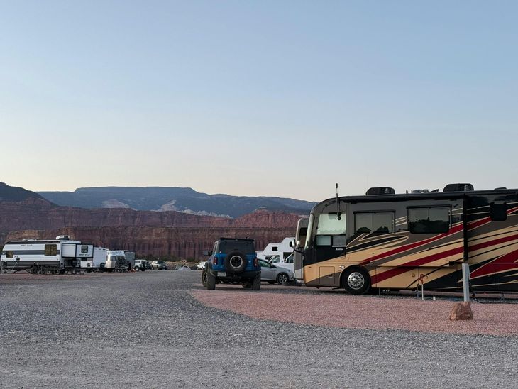 Interior of a caravan with a kitchen, seating area, and bed. Light wood cabinetry and warm color scheme.