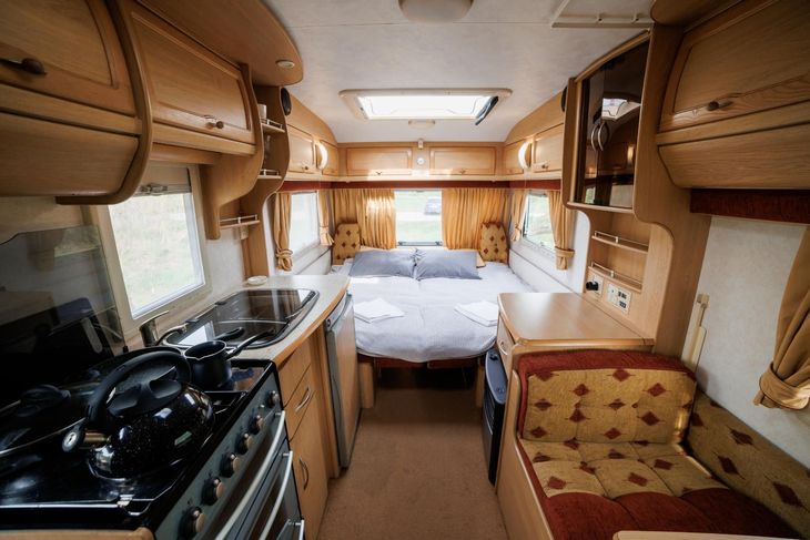 Cozy camper van interior with a bed, kitchen stove, wood cabinets, and a cushioned seat