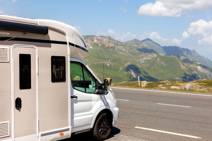 White RV parked on a road overlooking a mountain range.