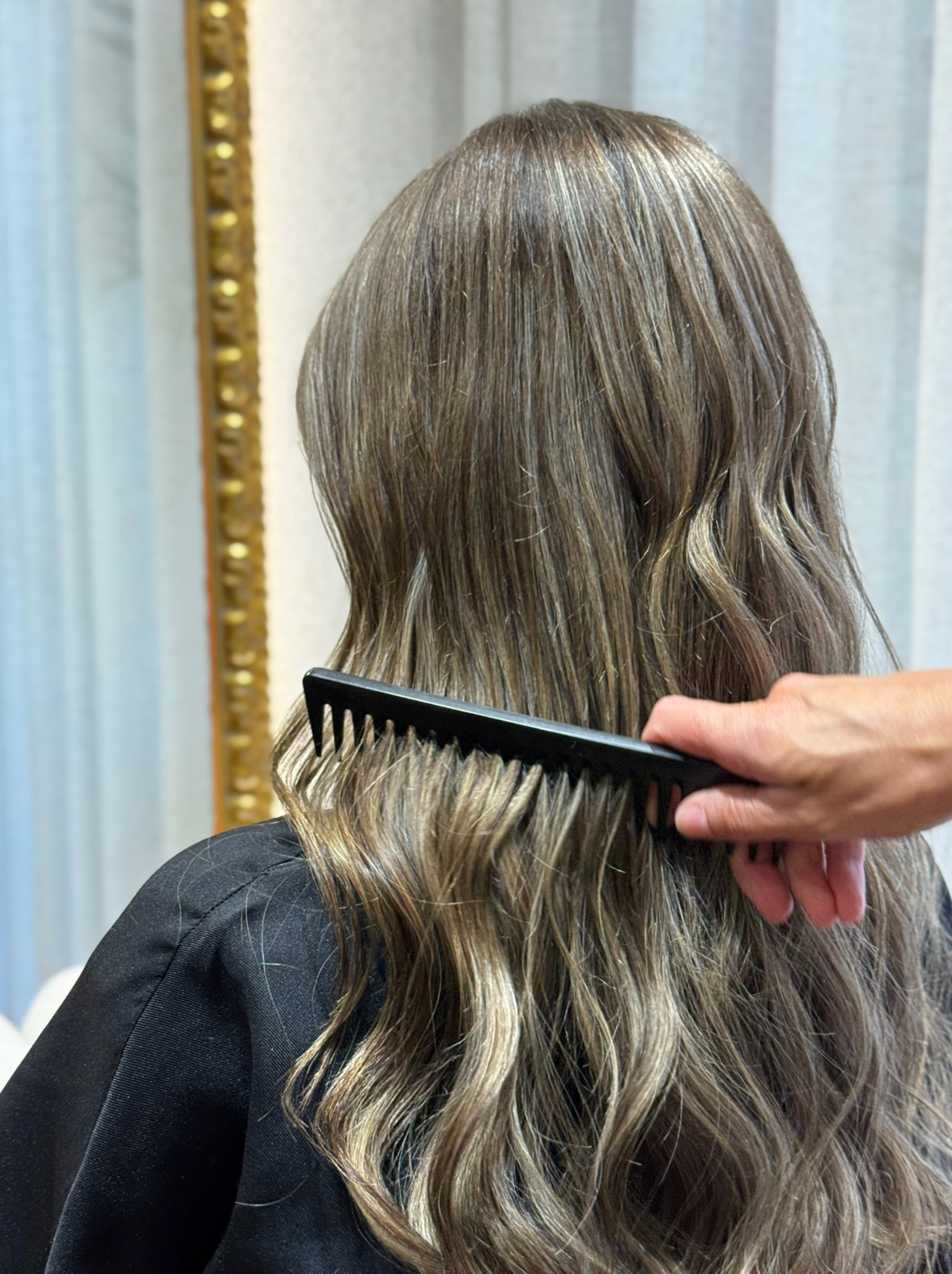 Una mujer está siendo peinada por un peluquero en un salón.