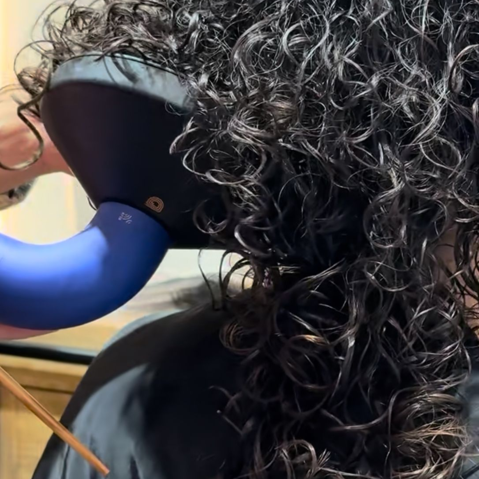 Una mujer con cabello rizado sonríe y mira a la cámara.