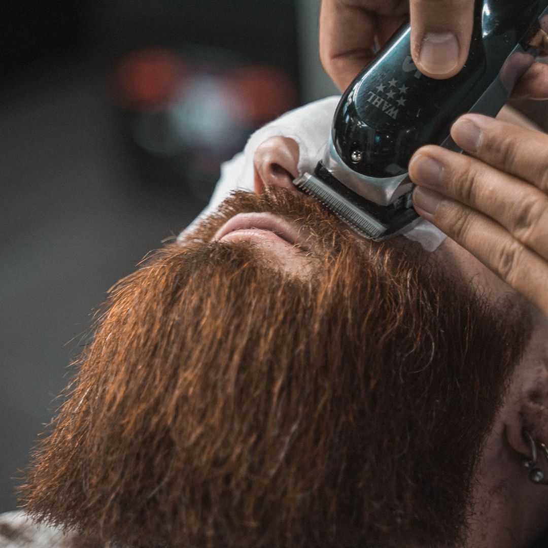 A un hombre le están recortando la barba con una maquinilla.