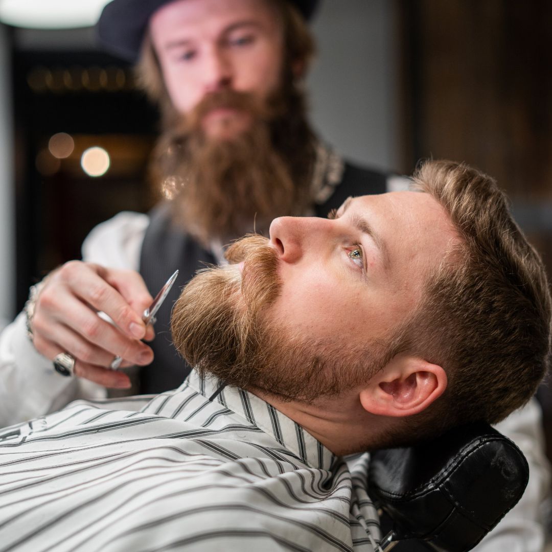 Un barbero le afeita la barba a un hombre con barba