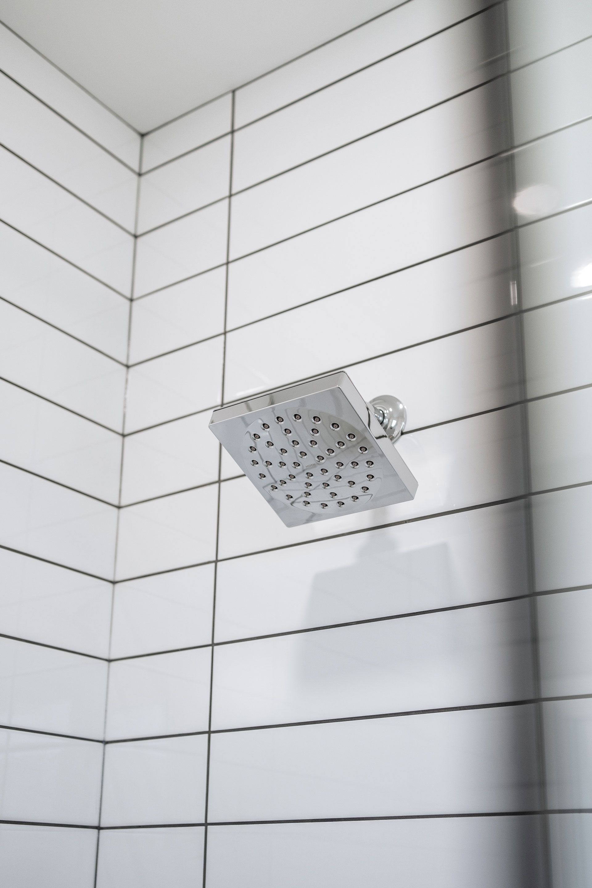 A shower head in a bathroom with white tiles Fidelity Homes Signature build in Brighton Township