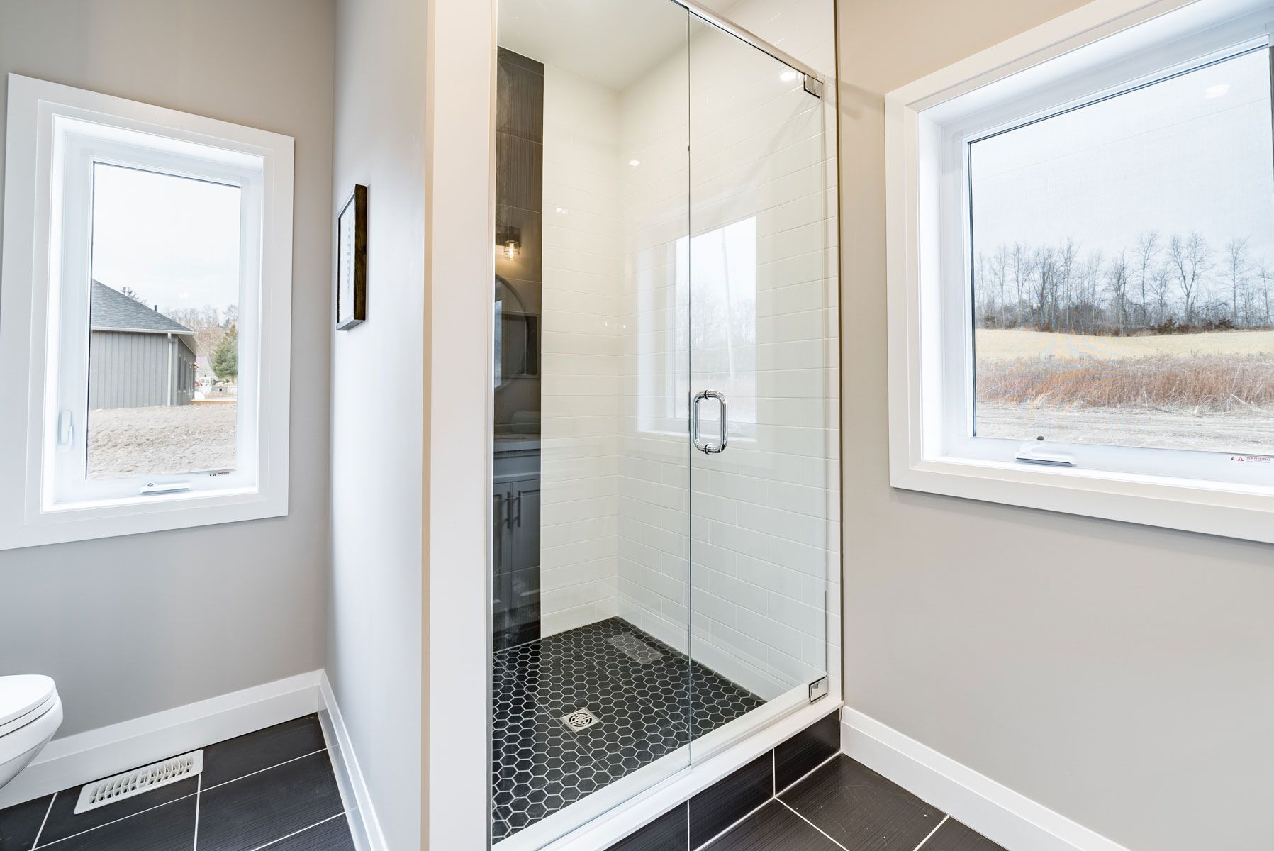 A bathroom with a walk in shower and two windows Fidelity Homes Signature build in Cramahe Township