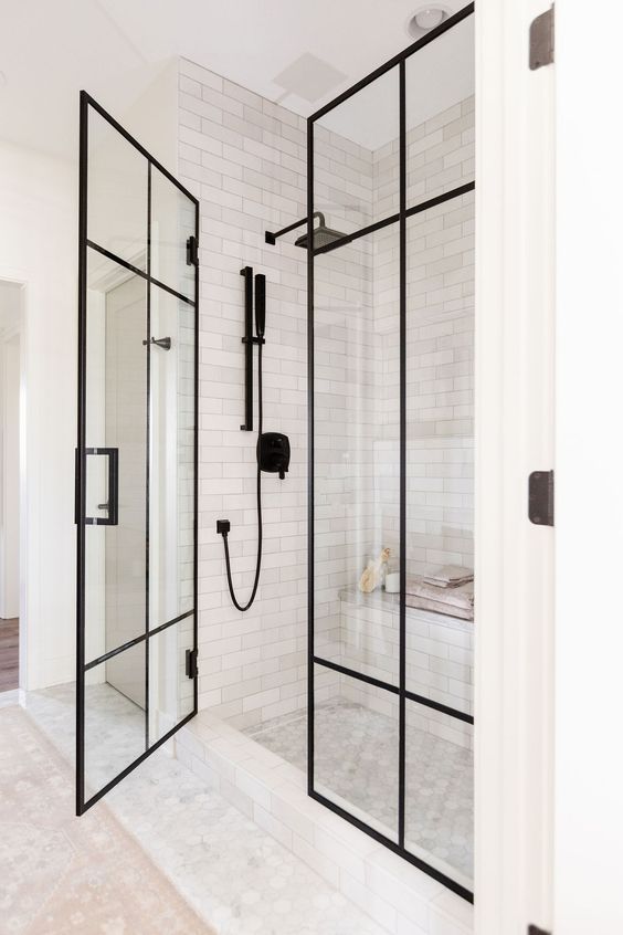 A bathroom with a walk in shower with black glass doors