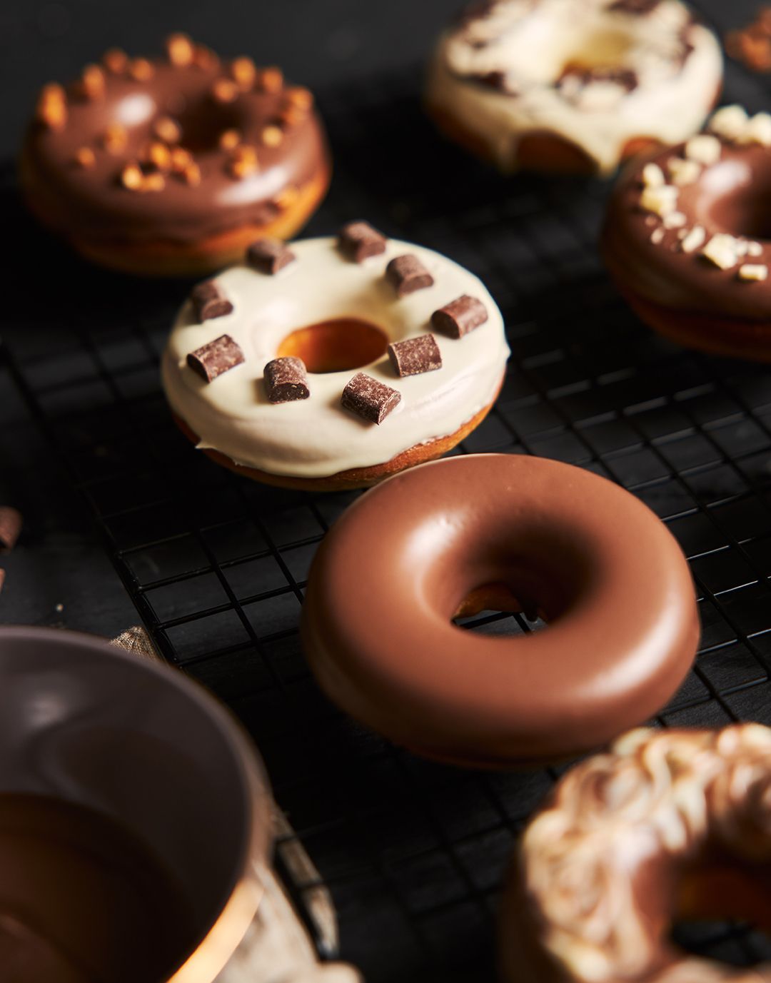 A variety of donuts are sitting on a cooling rack